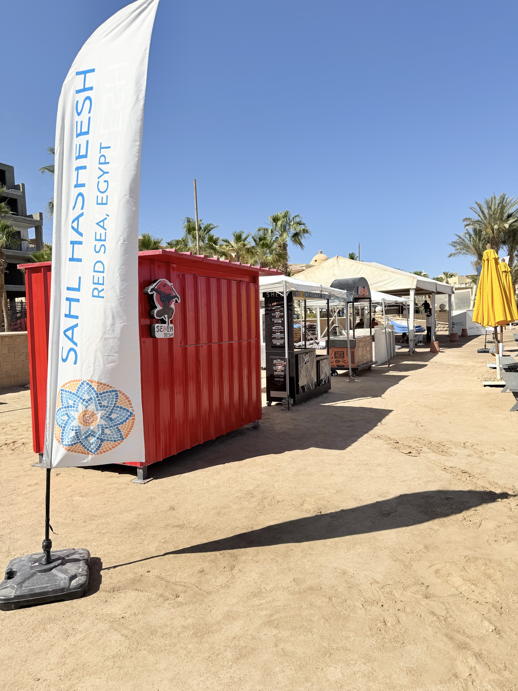 Food carts and kiosks alongside Sahl Hasheesh branded flags at the beach