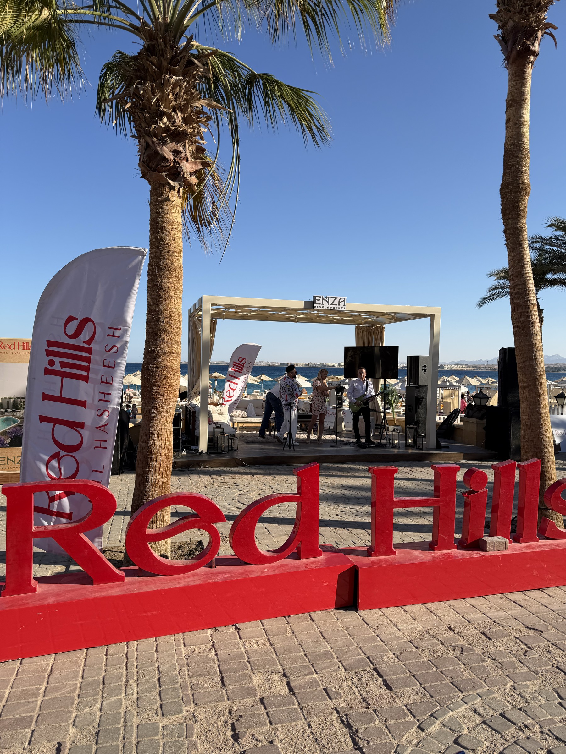 Musicians at the ENZA beachfront lounge behind large red Red Hills letters and branded flags